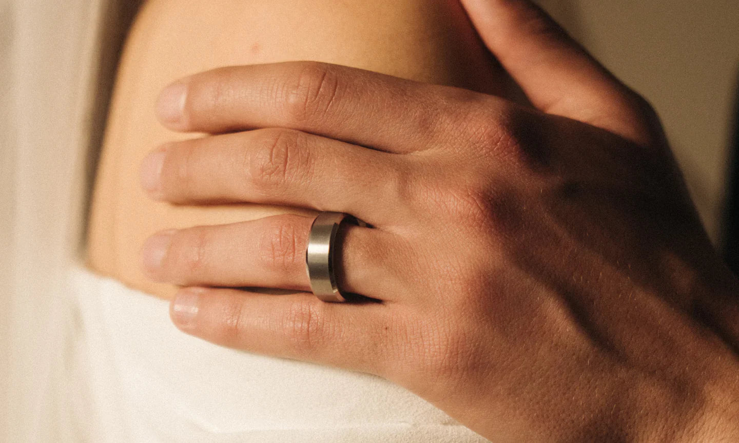 Mans hand resting on top of his brides shoulder. He is wearing a men's silver tungsten wedding band