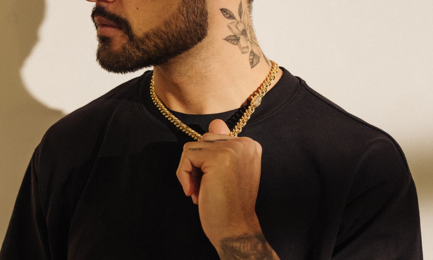 Man in a plain black t-shirt styling a gold cuban link chain