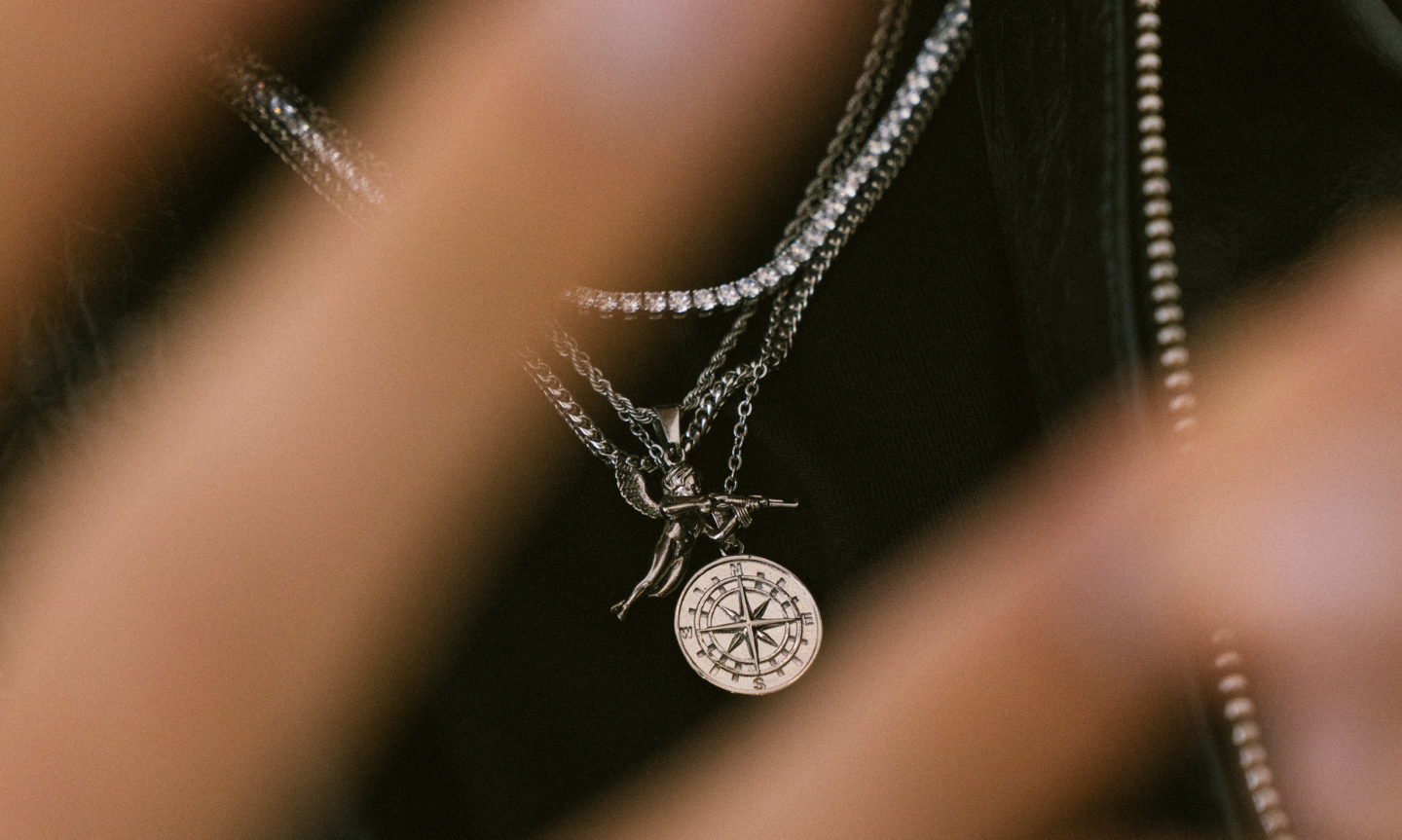 Close up shot of man's chest wearing a plain black t-shirt and silver jewellery including necklaces and chains