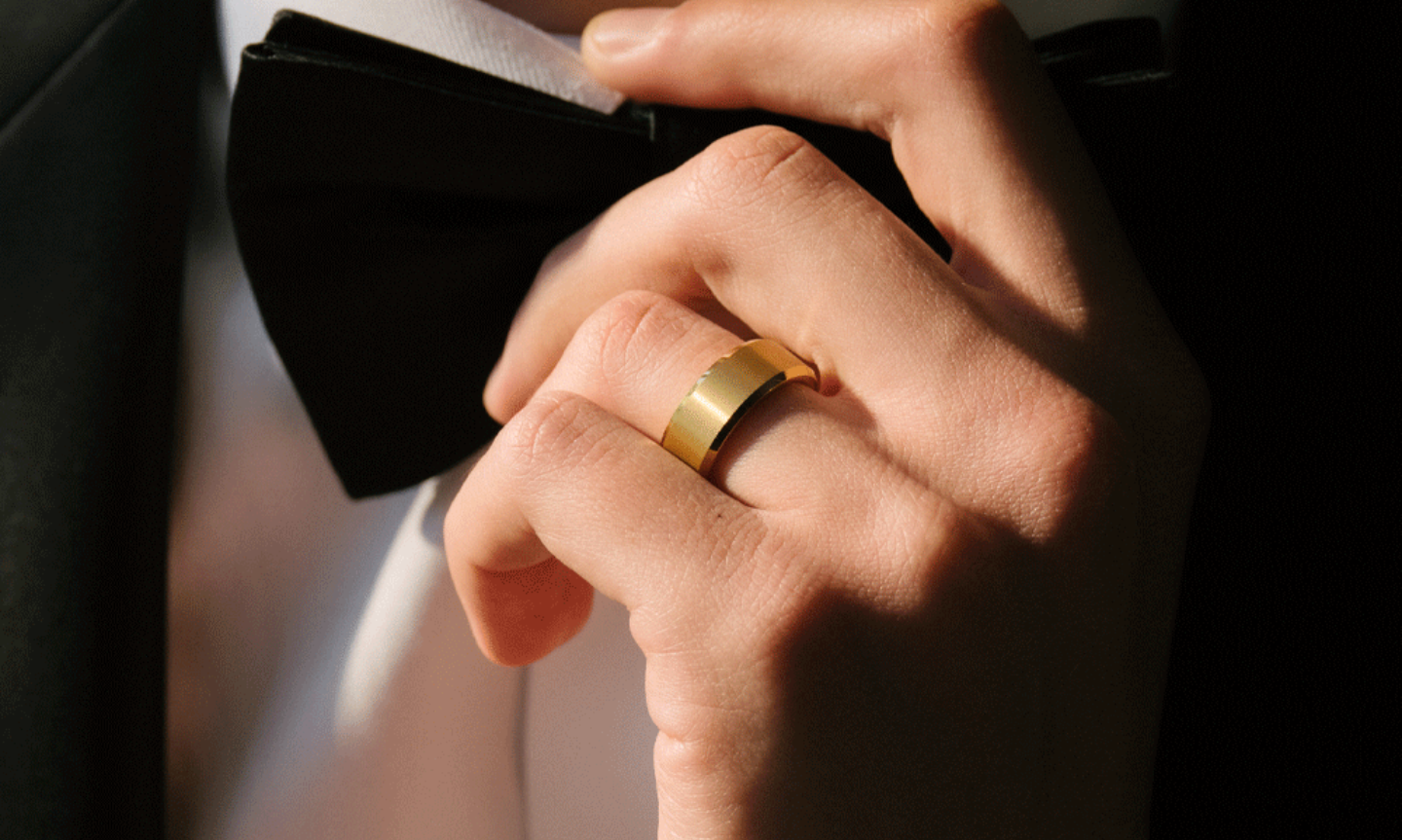 Man's hand touching his bow tie on his wedding day. He's wearing at 18ct gold tungsten wedding ring with a comfort fit band